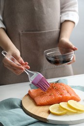 Photo of Woman marinating salmon fillet in dish at table, closeup