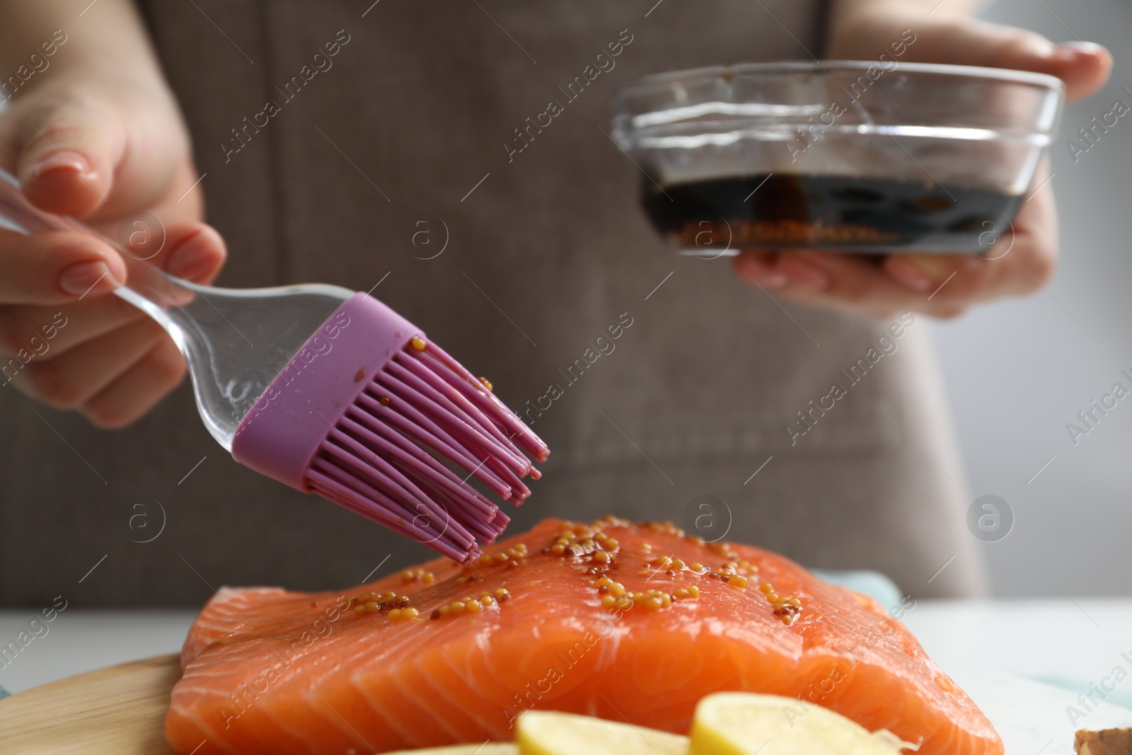 Photo of Woman marinating salmon fillet in dish at table, closeup