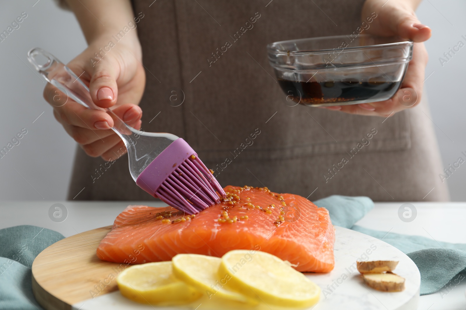 Photo of Woman marinating salmon fillet in dish at table, closeup