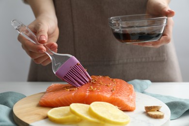 Photo of Woman marinating salmon fillet in dish at table, closeup