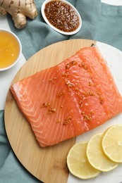 Photo of Salmon fillet with mustard, lemon slices, honey and ginger on table, flat lay