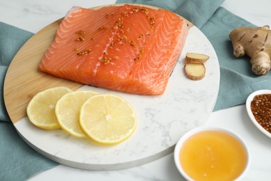 Photo of Salmon fillet with mustard, lemon slices, honey and ginger on white table, closeup