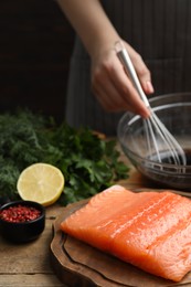 Photo of Woman making soy marinade for salmon fillet at wooden table, closeup