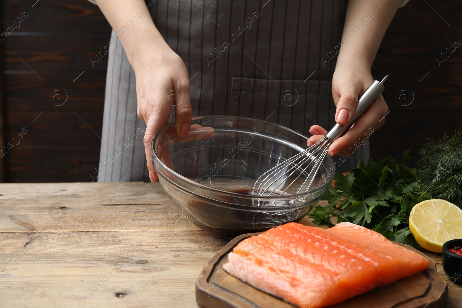 Photo of Woman making soy marinade for salmon fillet at wooden table, closeup