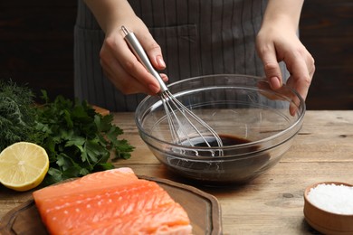 Photo of Woman making soy marinade for salmon fillet at wooden table, closeup