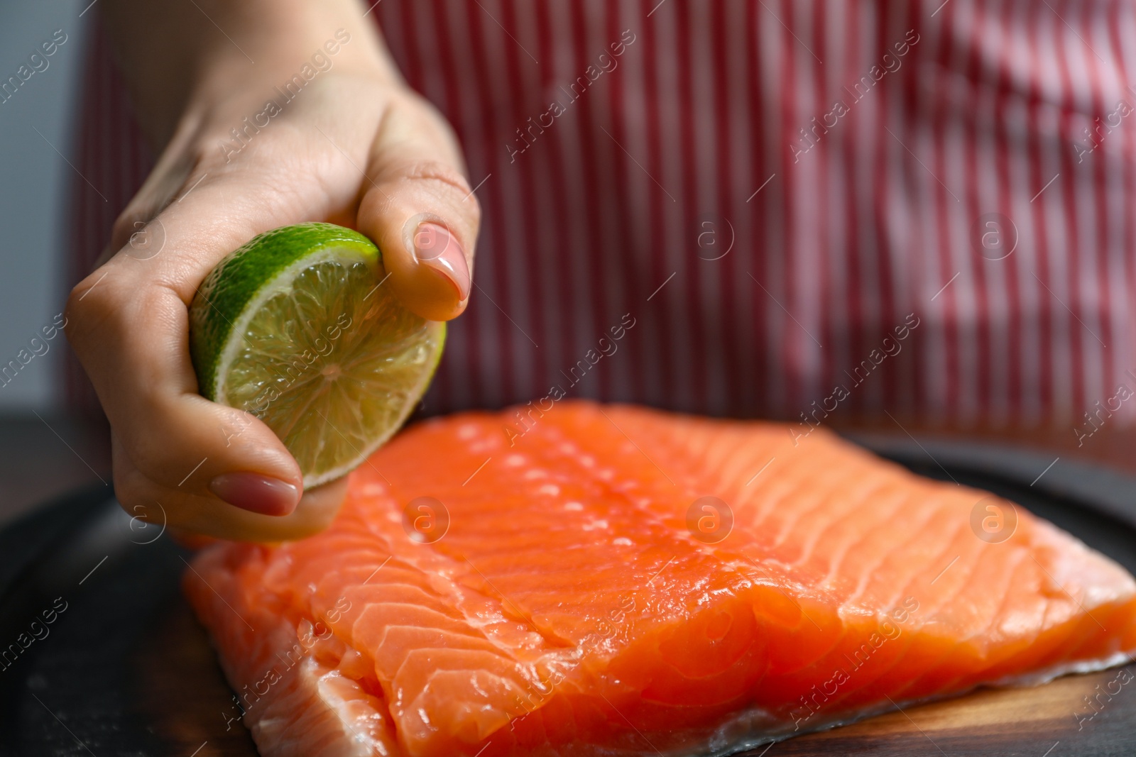 Photo of Woman squeezing lime juice onto salmon fillet at table, closeup