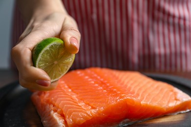 Woman squeezing lime juice onto salmon fillet at table, closeup