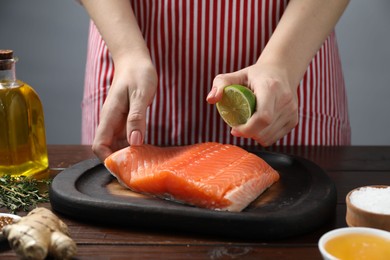 Photo of Woman squeezing lime juice onto salmon fillet at wooden table, closeup