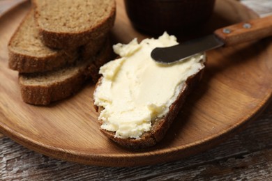 Photo of Fresh bread with butter and knife on wooden table, closeup