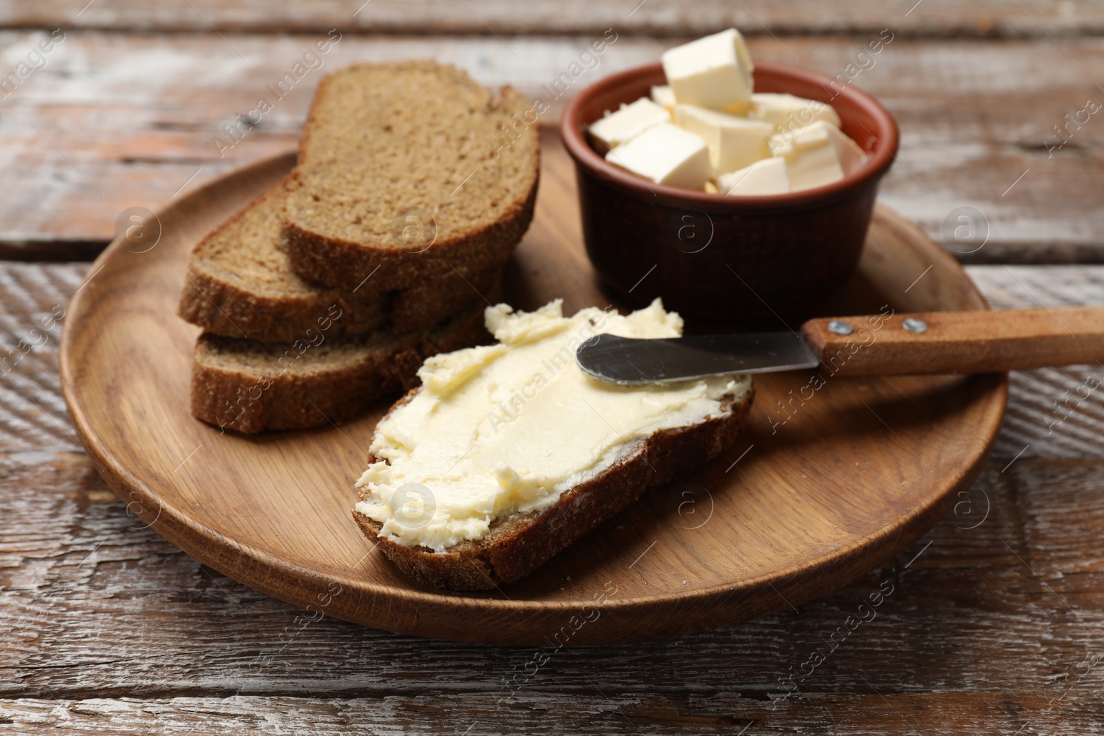 Photo of Fresh bread with butter and knife on wooden table, closeup