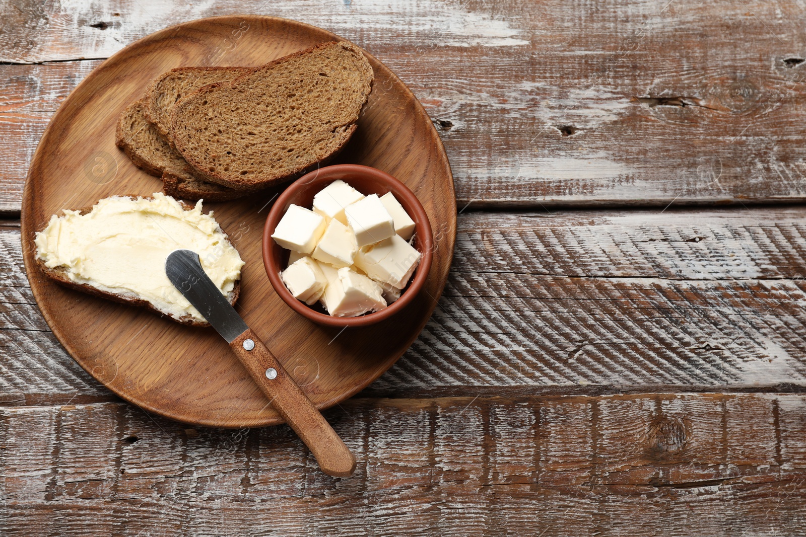 Photo of Fresh bread with butter and knife on wooden table, top view. Space for text