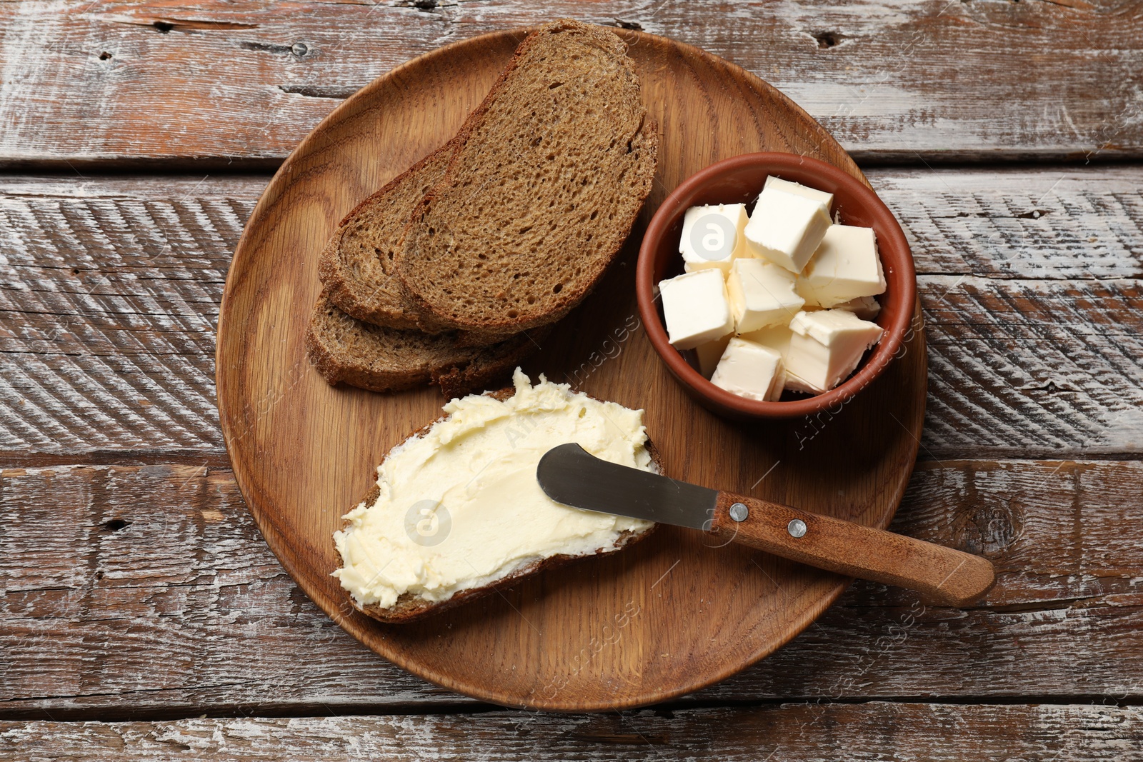 Photo of Fresh bread with butter and knife on wooden table, top view