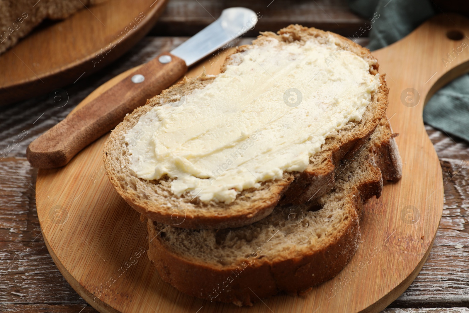 Photo of Fresh bread with butter and knife on wooden table, closeup