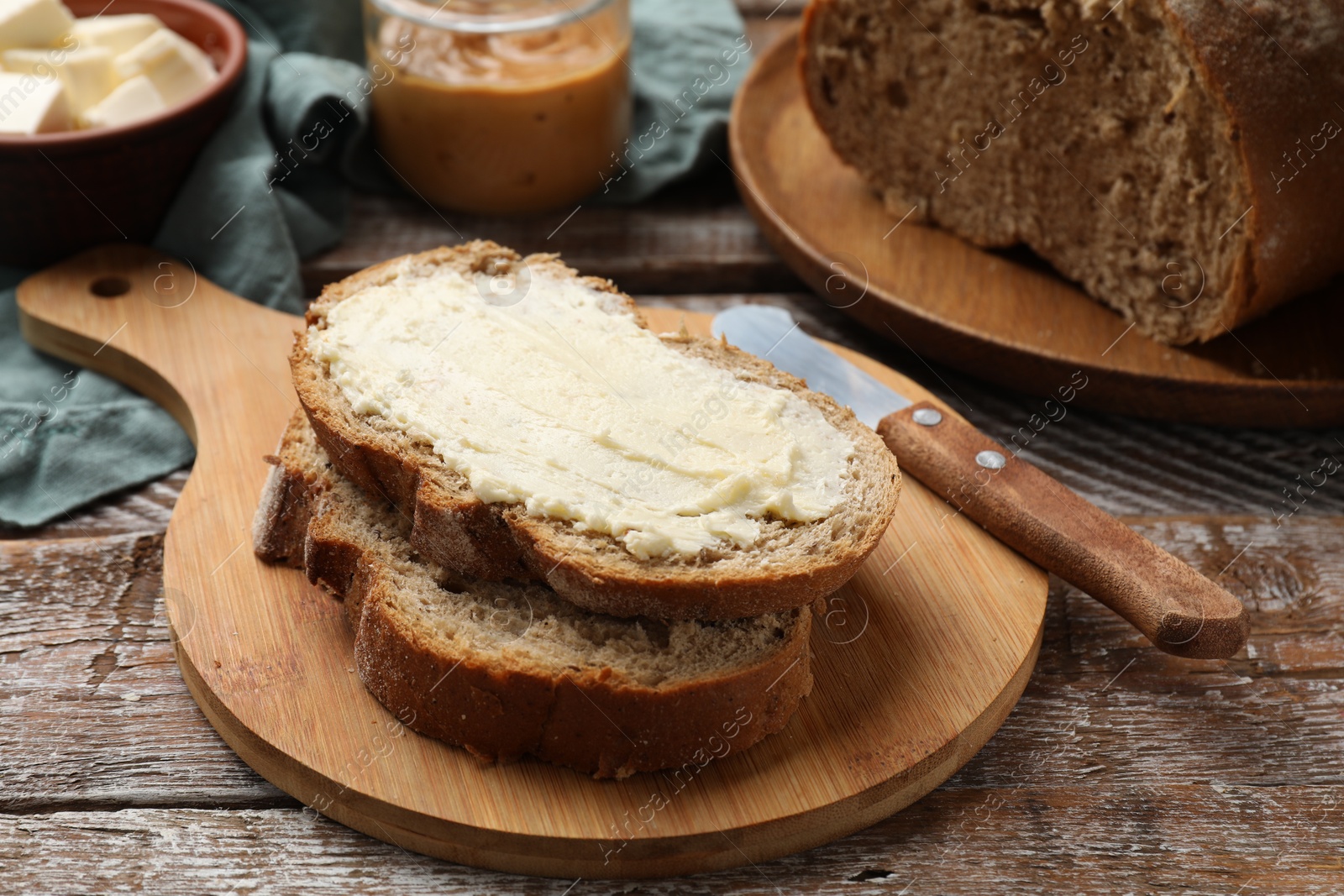 Photo of Fresh bread with butter and knife on wooden table, closeup