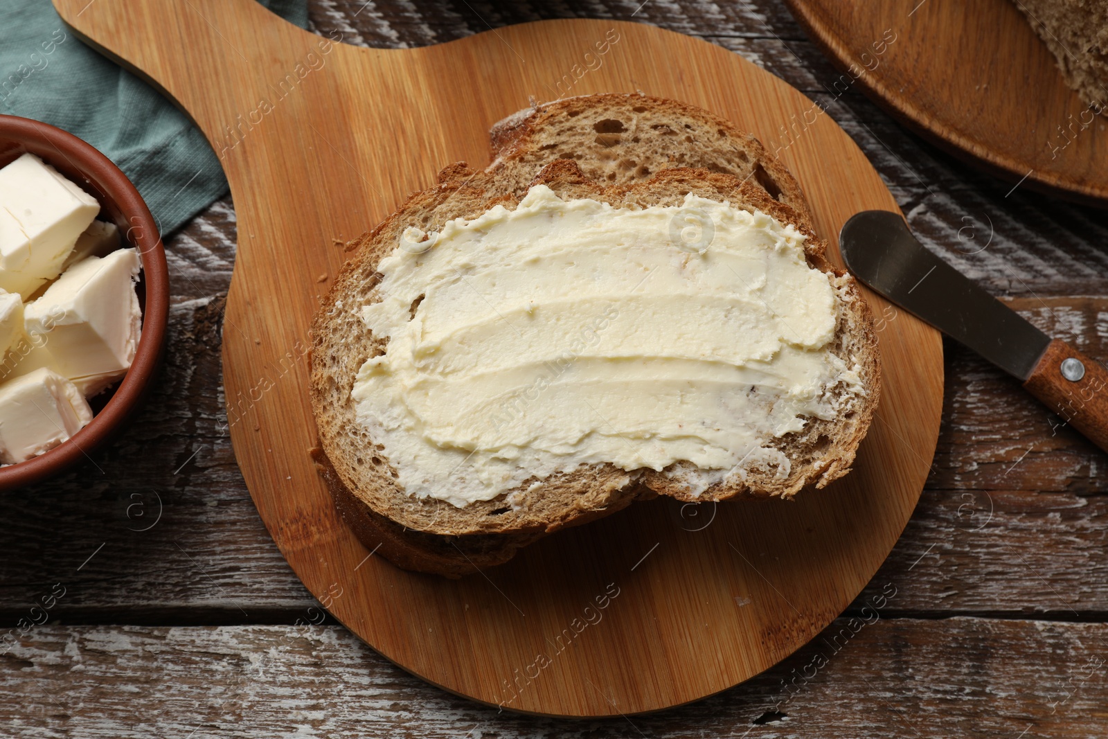 Photo of Fresh bread with butter and knife on wooden table, flat lay