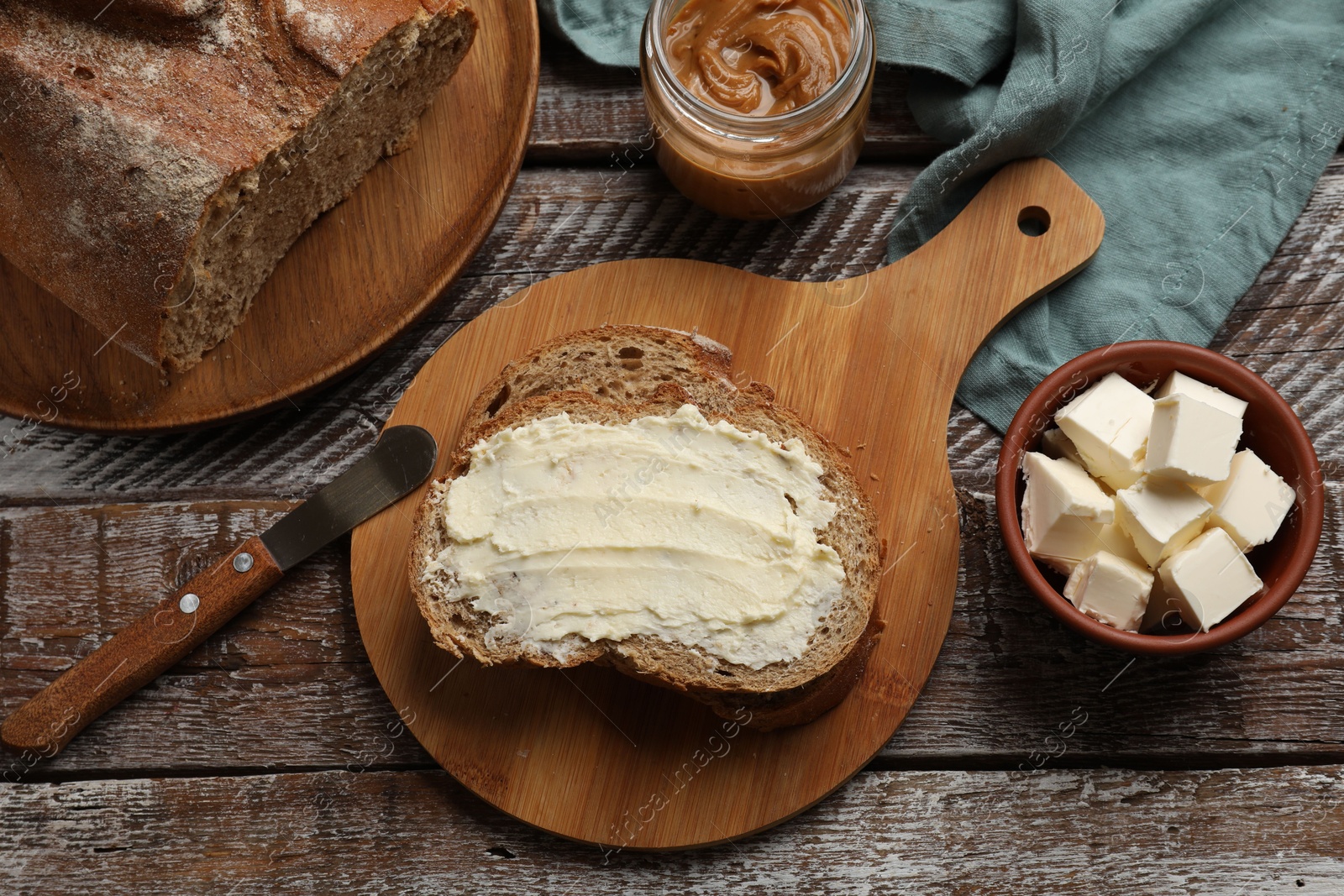 Photo of Fresh bread with butter and knife on wooden table, flat lay