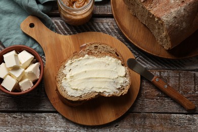 Photo of Fresh bread with butter and knife on wooden table, flat lay