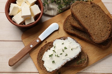 Photo of Fresh bread with butter, thyme and knife on light wooden table, flat lay