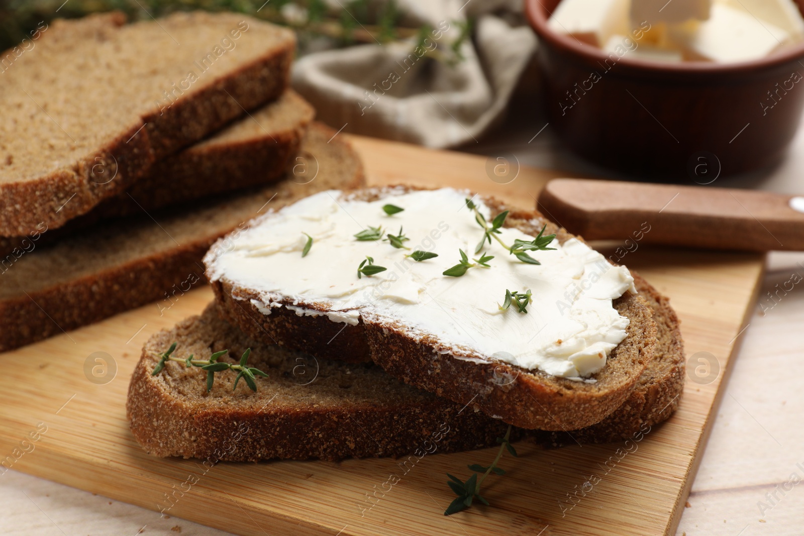 Photo of Fresh bread with butter, thyme and knife on light table, closeup