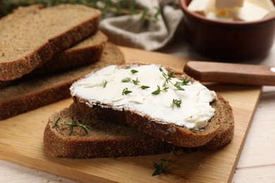 Photo of Fresh bread with butter, thyme and knife on light table, closeup