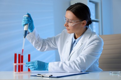 Photo of Laboratory testing. Doctor dripping blood sample into test tube at table indoors