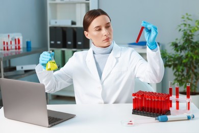 Laboratory testing. Doctor with blood sample in tube and flask at table indoors