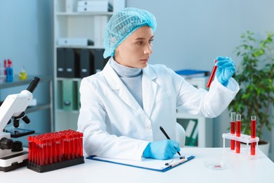 Laboratory testing. Doctor with blood sample taking notes at table indoors