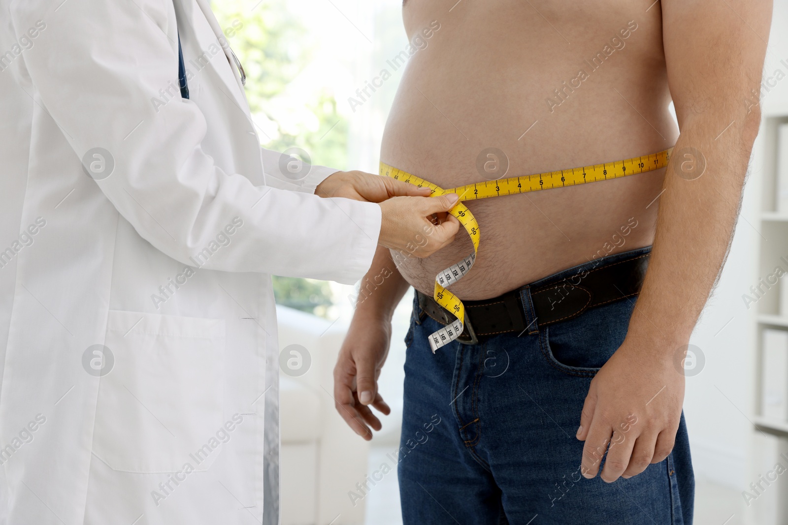 Photo of Nutritionist measuring overweight man's waist with tape in clinic, closeup