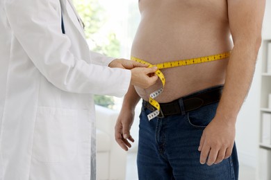 Photo of Nutritionist measuring overweight man's waist with tape in clinic, closeup