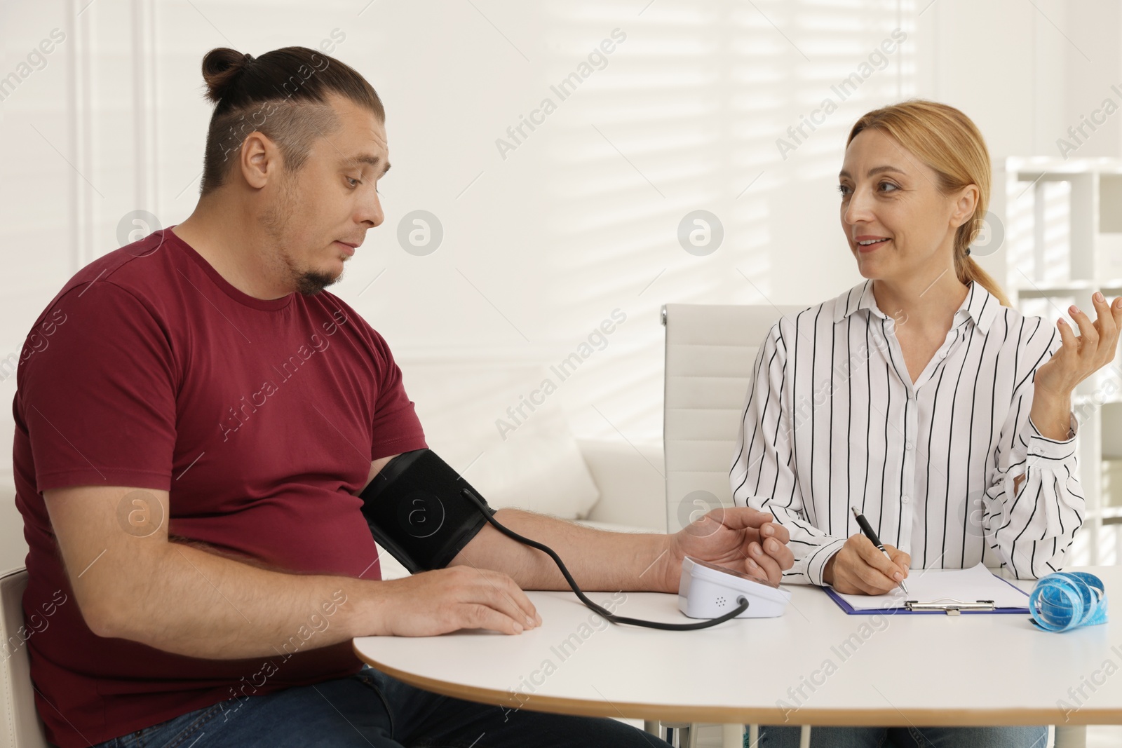 Photo of Nutritionist measuring overweight patient's blood pressure at table in clinic