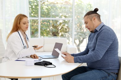 Nutritionist consulting overweight man at table in clinic