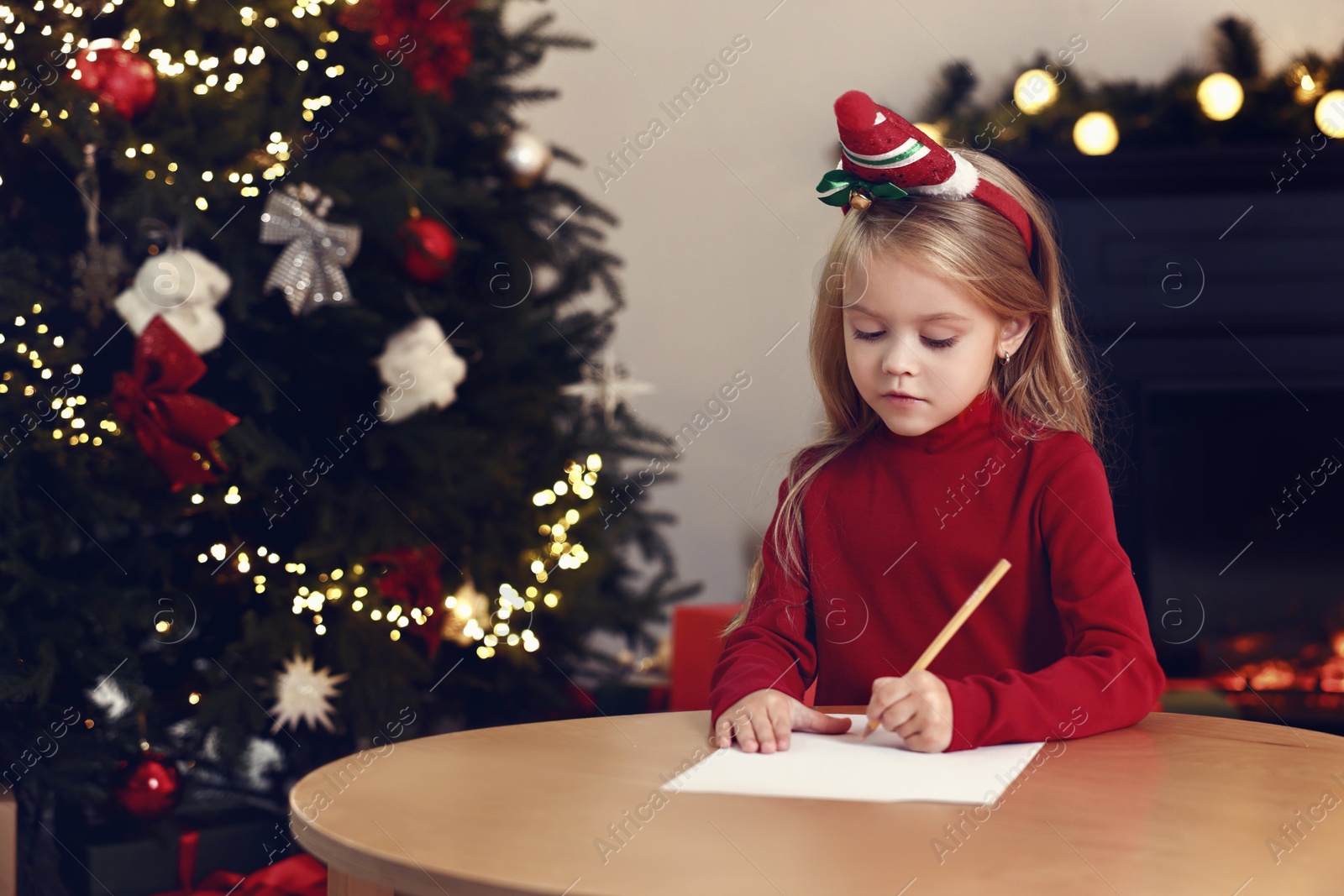 Photo of Little girl writing letter to Santa Claus at table indoors. Christmas celebration