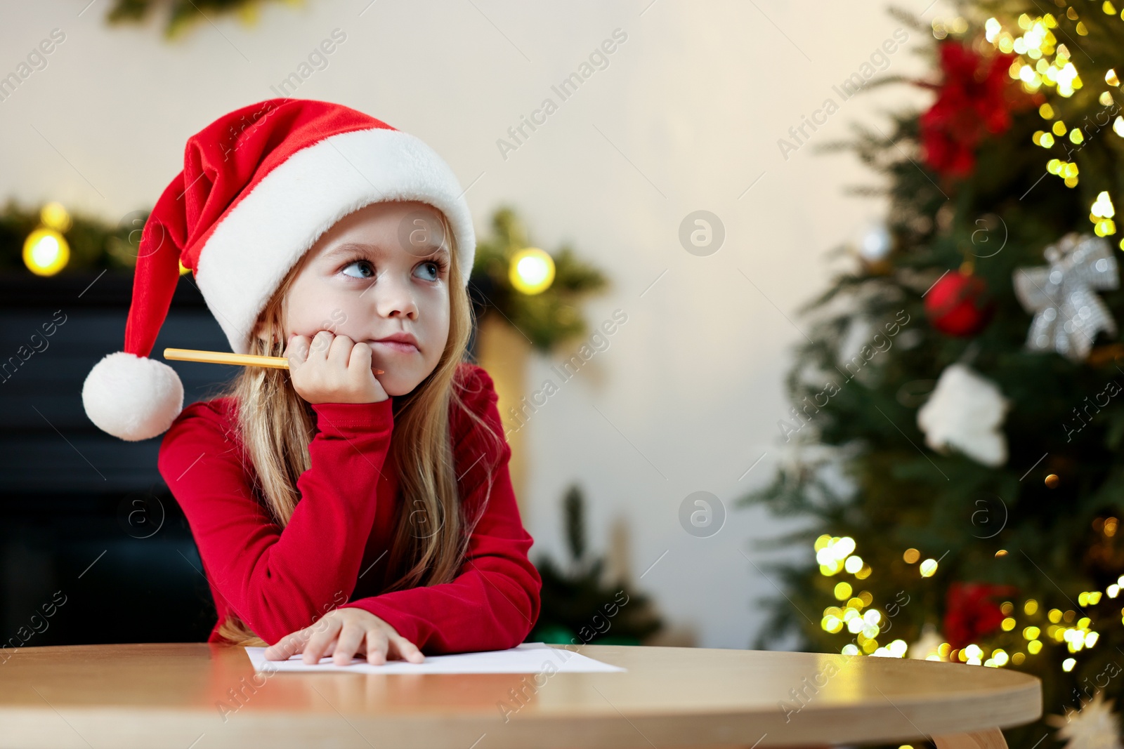 Photo of Little girl writing letter to Santa Claus at table indoors. Christmas celebration