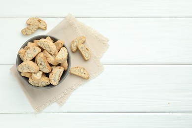 Photo of Traditional Italian almond biscuits (Cantucci) in bowl on white wooden table, top view. Space for text