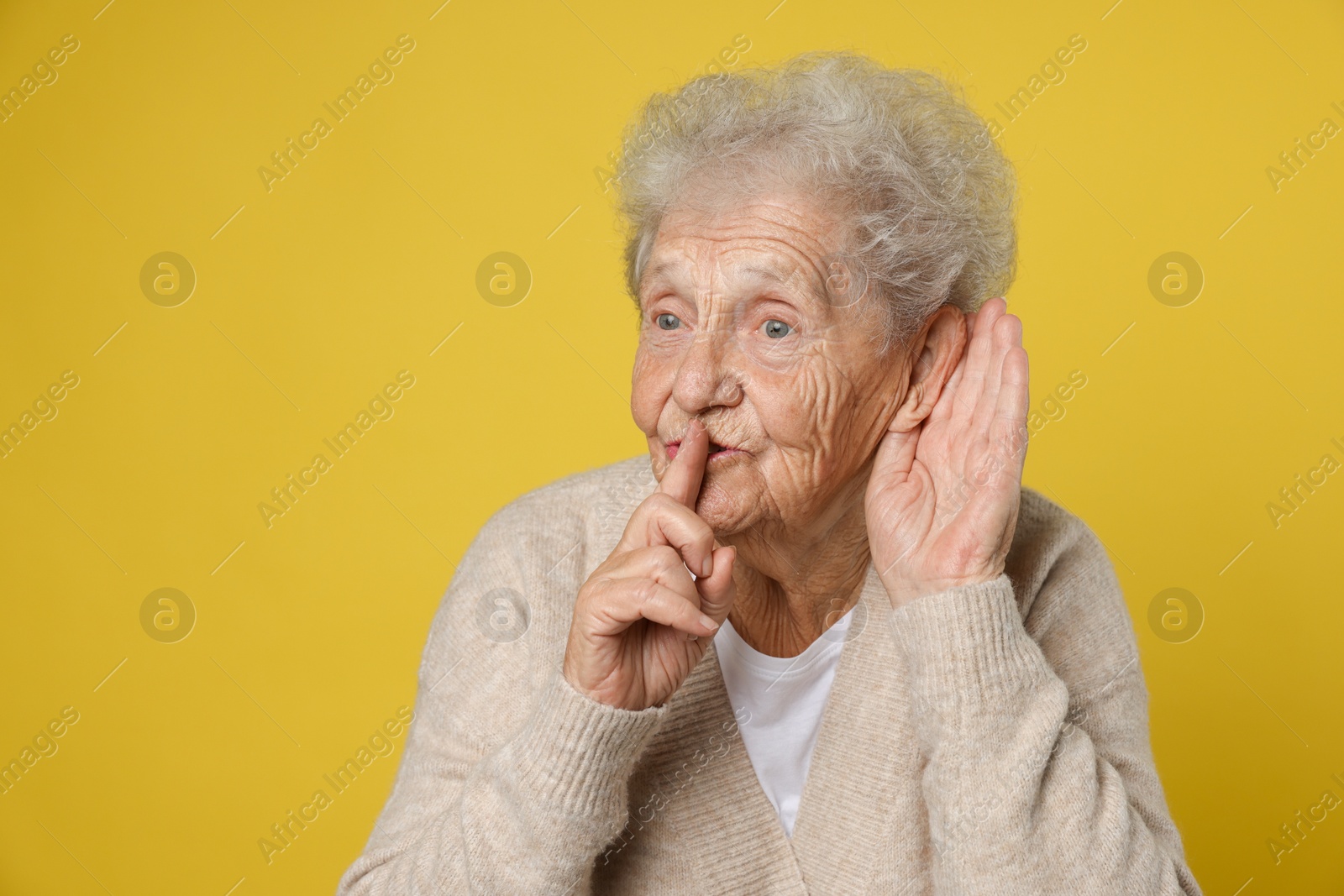 Photo of Senior woman showing hand to ear gesture on dark yellow background