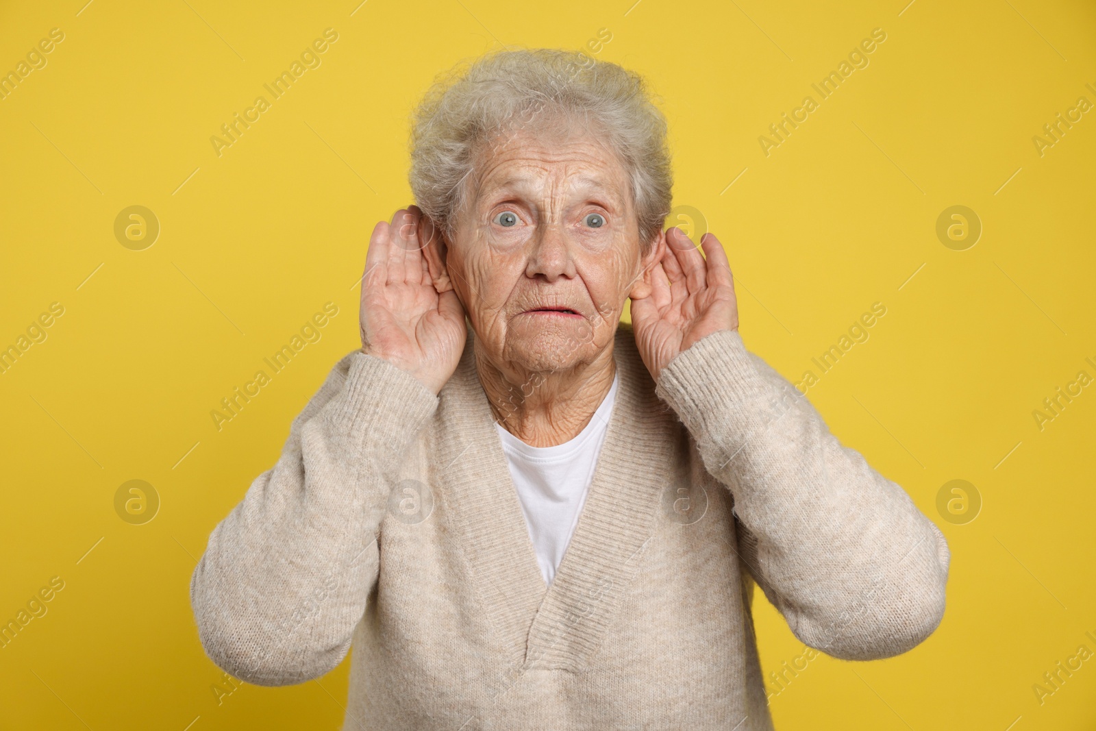 Photo of Senior woman showing hand to ear gesture on dark yellow background