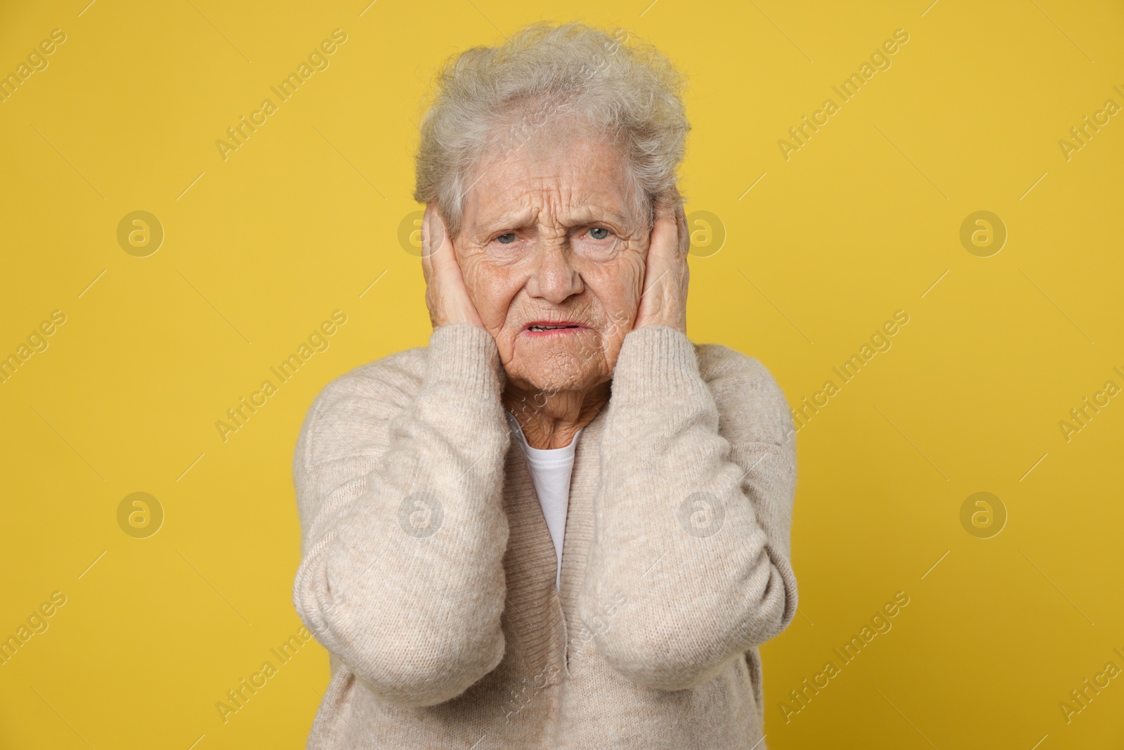 Photo of Senior woman covering her ears on dark yellow background