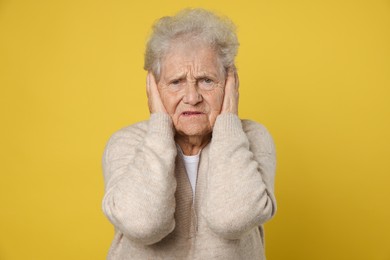 Senior woman covering her ears on dark yellow background