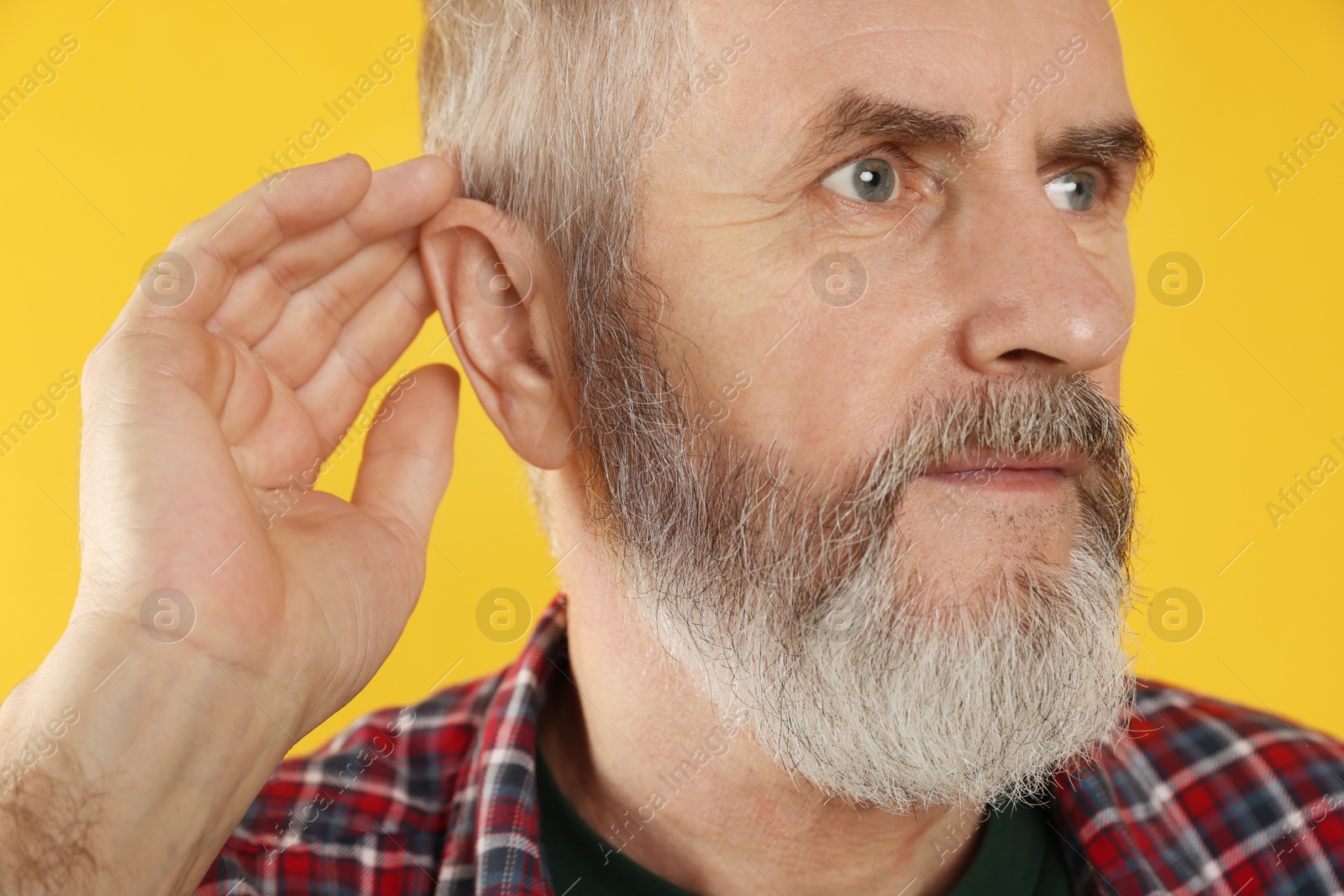 Photo of Senior man showing hand to ear gesture on orange background, closeup