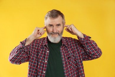 Photo of Senior man covering his ears with fingers on orange background