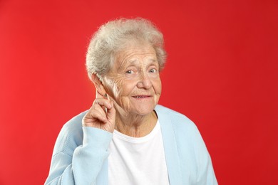 Senior woman showing hand to ear gesture on red background