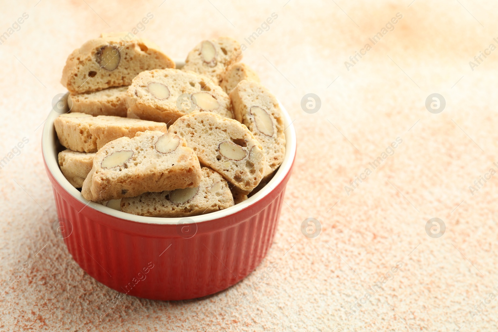 Photo of Traditional Italian almond biscuits (Cantucci) in bowl on beige textured table, closeup. Space for text