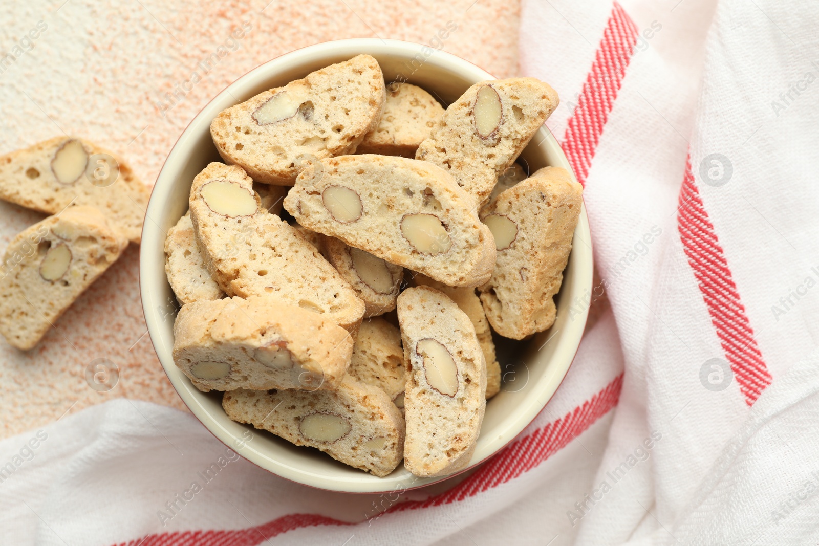 Photo of Traditional Italian almond biscuits (Cantucci) in bowl on beige textured table, top view