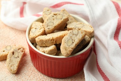 Traditional Italian almond biscuits (Cantucci) in bowl on beige textured table, closeup