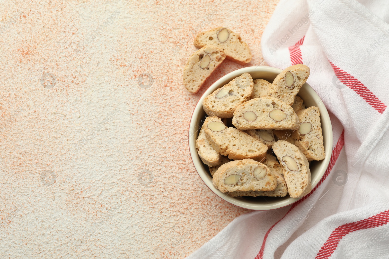 Photo of Traditional Italian almond biscuits (Cantucci) in bowl on beige textured table, top view. Space for text