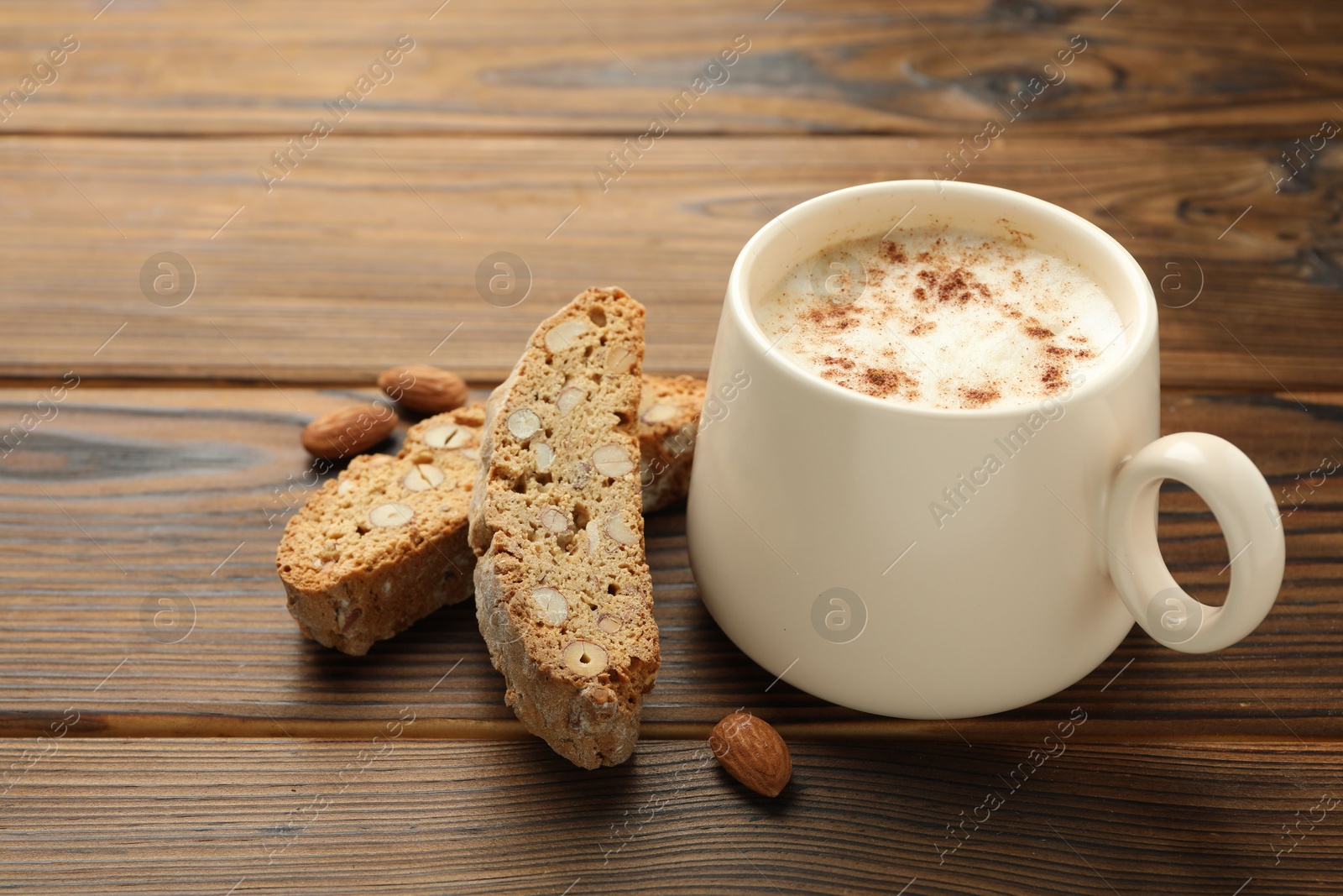 Photo of Traditional Italian almond biscuits (Cantucci), nuts and cup of coffee on wooden table, closeup