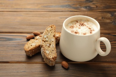 Traditional Italian almond biscuits (Cantucci), nuts and cup of coffee on wooden table, closeup