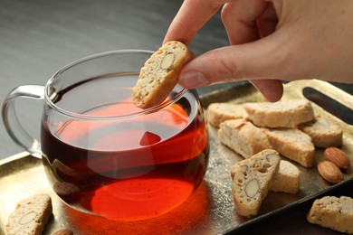 Woman dipping traditional Italian almond biscuit (Cantucci) into cup of tea at table, closeup