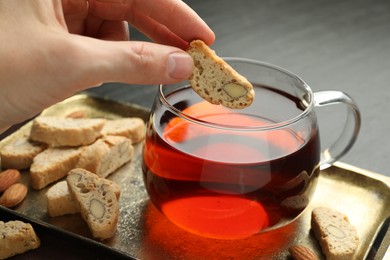 Photo of Woman dipping traditional Italian almond biscuit (Cantucci) into cup of tea at table, closeup