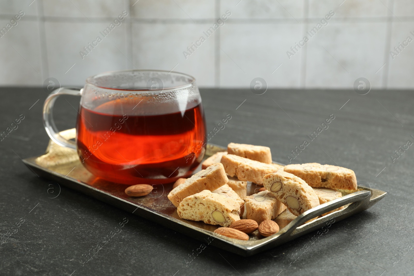 Photo of Traditional Italian almond biscuits (Cantucci), nuts and cup of tea on grey textured table, closeup